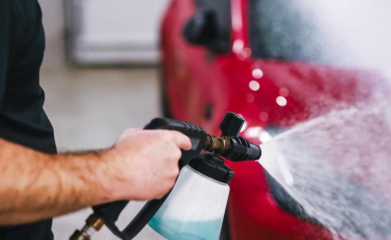 A vehicle detailing technician applying foam while washing a car